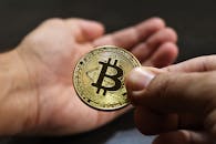 Close-up image showing hands exchanging a Bitcoin coin, symbolizing cryptocurrency transactions.